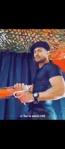 a man wearing a hat and a watch is holding a remote control and says " tap to watch live " on the bottom
