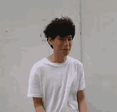 a young man in a white t-shirt is holding a cell phone in his hands .