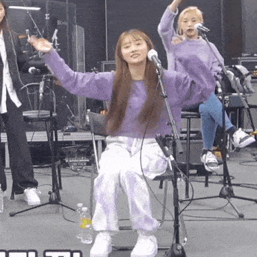 a woman in a purple sweater sits in front of a microphone with her arms outstretched