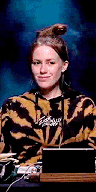 a woman in a tie dye hoodie is sitting in front of a laptop computer .
