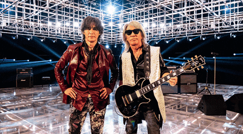 two men standing next to each other one holding a guitar