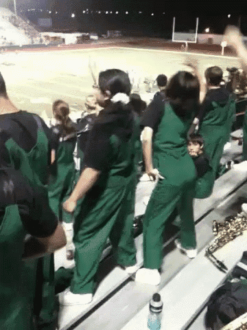 a group of people in green overalls are standing in a stadium watching a football game