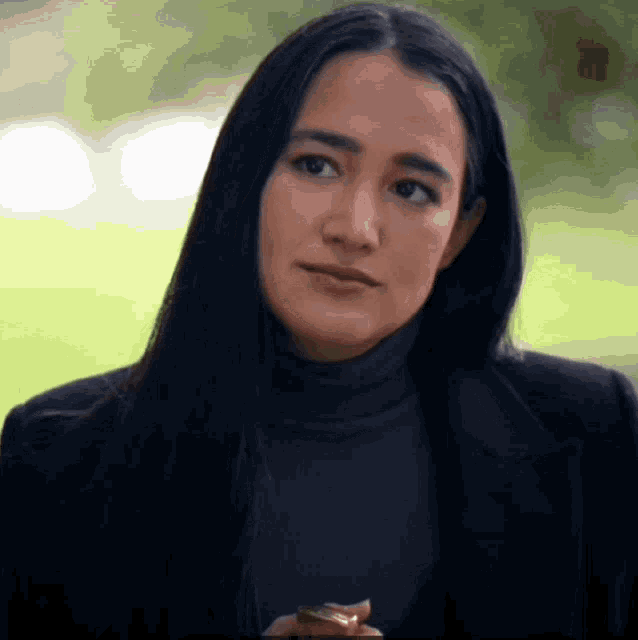 a woman with long dark hair wearing a black turtleneck and black jacket