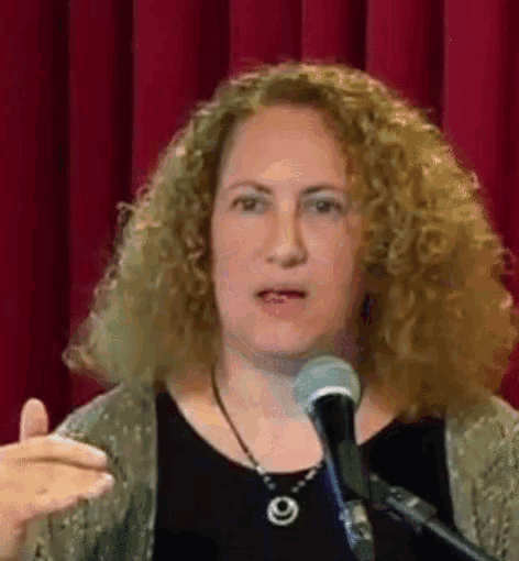 a woman with curly hair is speaking into a microphone in front of a red curtain