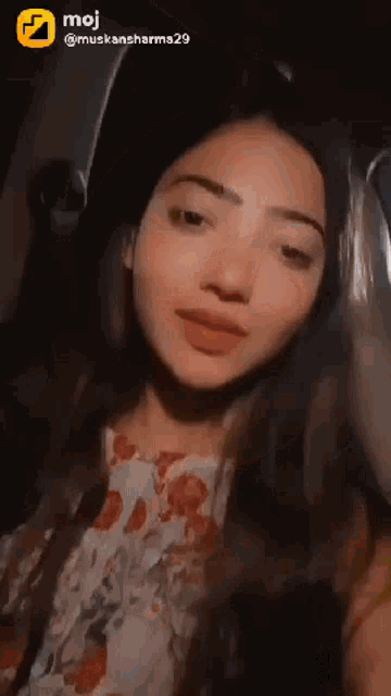 a woman is taking a selfie in a car with a moji logo in the corner