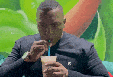 a man wearing a black shirt with the letter x on it drinks from a cup with a straw
