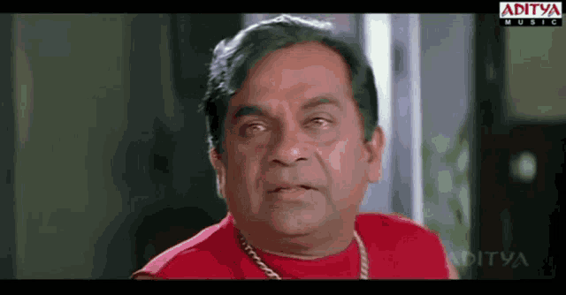 a man is wearing a red shirt with a gold chain around his neck and a logo for aditya music