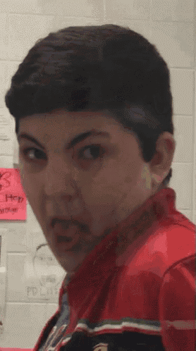 a boy in a red jacket is making a funny face in front of a wall with a sign that says " hey "