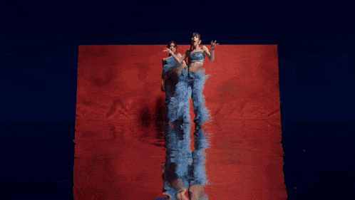a woman in a blue crop top and feathered shorts is dancing on a red background