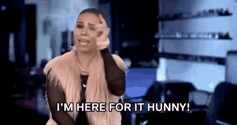 a woman in a fur vest is holding her hand to her head and saying `` i 'm here for it hunny '' .