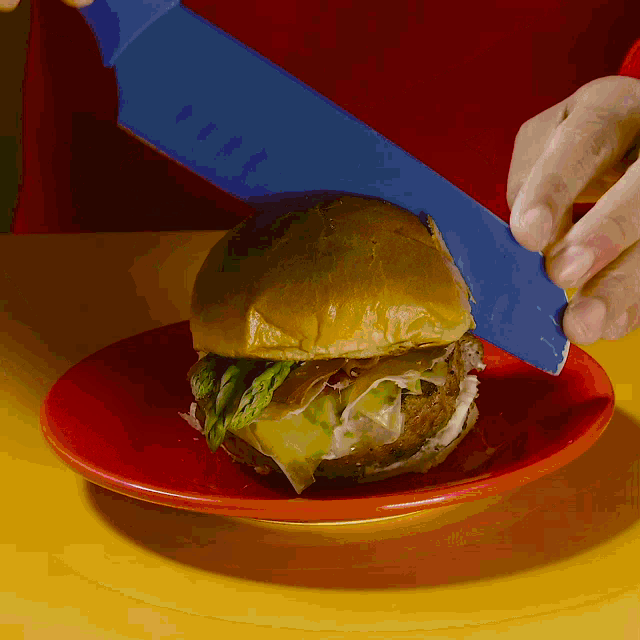 a person cutting a hamburger with a blue knife on a red plate