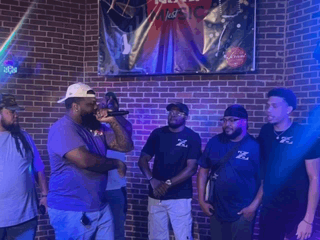 a group of men are standing in front of a brick wall with a sign that says " new music "