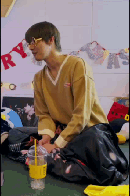 a man wearing glasses sits on the floor with a cup of coffee in front of a banner that says ry