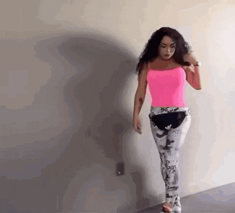 a woman in a pink tank top and gray pants is walking against a wall .