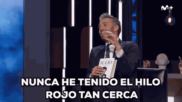 a man in a suit and tie is holding a book and saying nunca he tenido el hilo rojo tan cerca