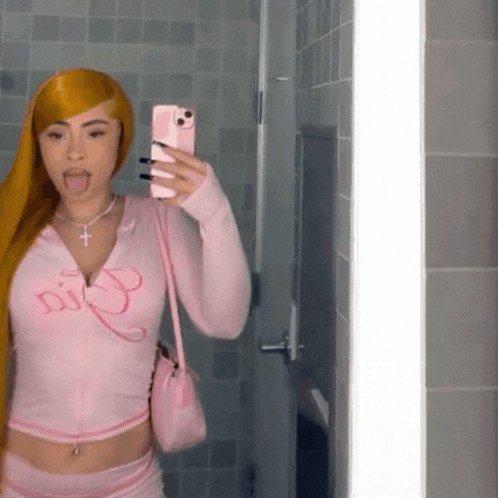 a woman taking a selfie in front of a mirror wearing a pink shirt that says dior