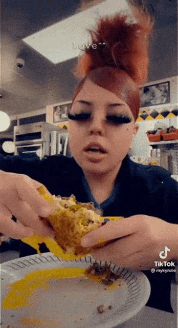 a woman with red hair is eating a taco from a paper plate with a tik tok watermark