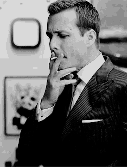 a man in a suit is smoking a cigarette in a black and white photo