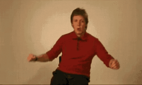 a man in a red shirt is sitting on a chair and dancing .