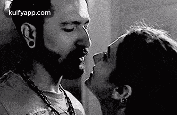 a black and white photo of a man and a woman kissing .