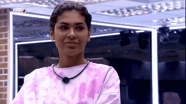 a woman wearing a pink tie dye shirt and a black necklace is smiling .