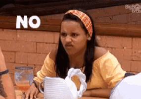 a woman is sitting at a table with a pitcher of water and a sign that says no on the wall behind her .