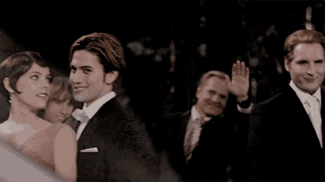 a man in a tuxedo is waving to a woman in a pink dress
