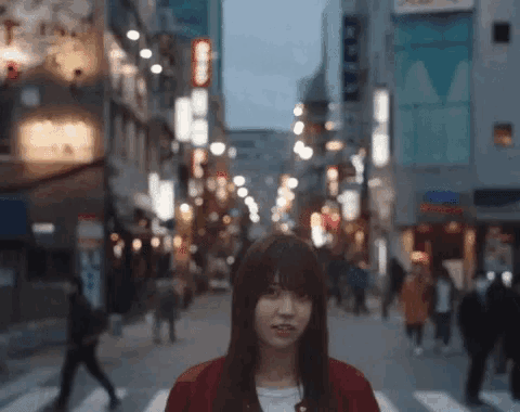 a woman in a red jacket stands in front of a busy street with a sign that says ' coca cola ' on it