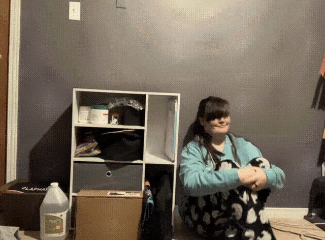 a woman sits on the floor in front of a shelf with a gallon of liquid in front of her