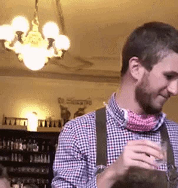 a man in a plaid shirt and suspenders is holding a drink