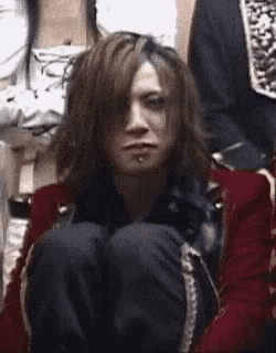 a man with long hair and a piercing in his nose is sitting on the floor with his legs crossed .