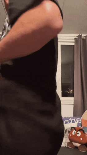 a man in a black shirt is standing in a room with a stuffed mario on the floor