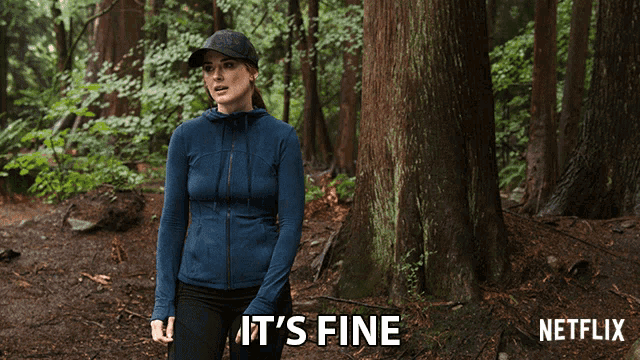 a woman in a blue jacket stands in the woods with the words it 's fine written below her