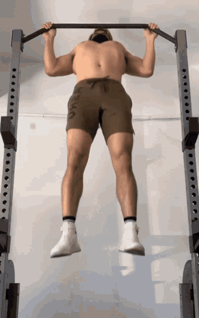 a shirtless man is doing a pull up while wearing shorts with the letter a on them