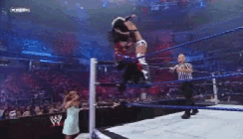 a woman is jumping over a man in a wrestling ring while a referee looks on .