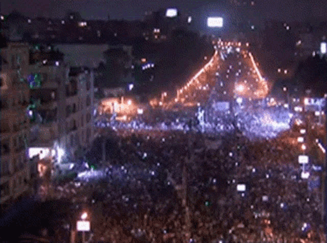 a large crowd of people are gathered in a city at night with a pyramid in the background