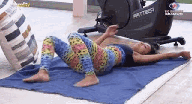 a woman is laying on a blue towel next to an exercise bike .