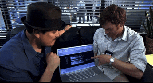 two men are looking at a laptop and one is pointing at a screen