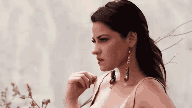 a woman wearing a pink dress and red earrings looks to the side