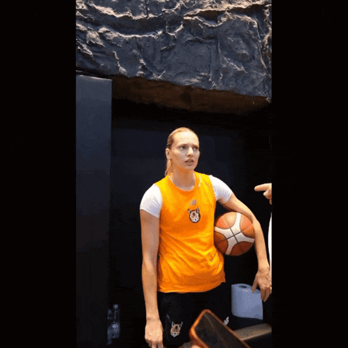 a woman wearing an orange shirt with a cat on it holds a basketball