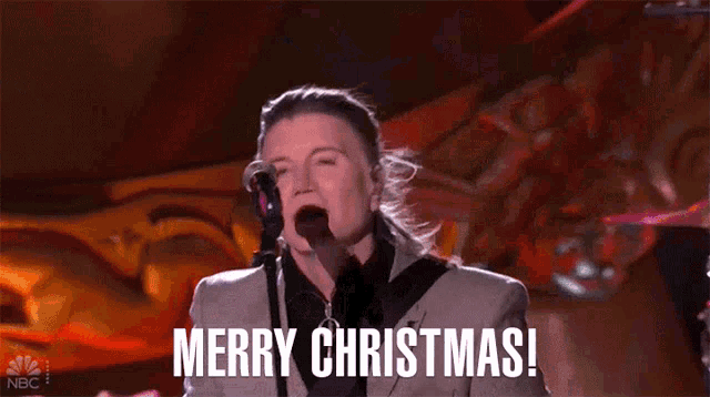 a man in a suit is singing into a microphone with the words merry christmas written below him .