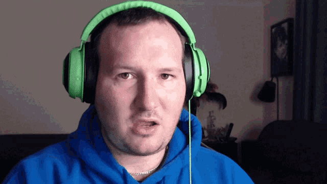 a man wearing a blue hoodie and green headphones makes a funny face