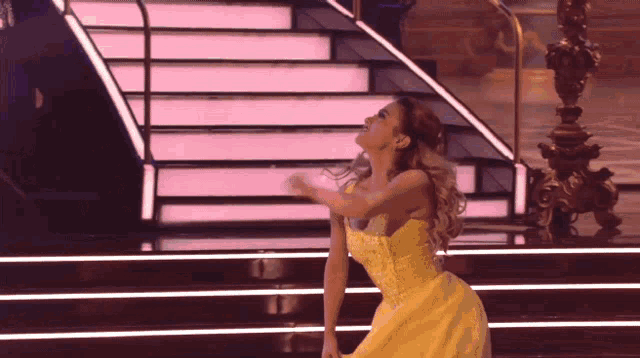 a woman in a yellow dress is dancing on a stage in front of stairs