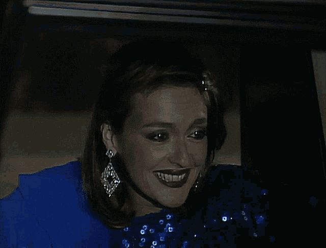 a woman in a blue dress and earrings smiles