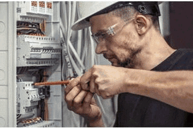 a man wearing a hard hat and safety glasses is working on an electric box .