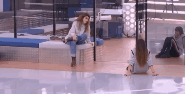 a woman sits on a bench while another woman sits on the floor behind her