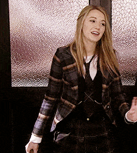 a woman wearing a plaid jacket and tie smiles while standing in front of a glass door