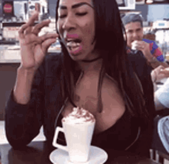 a woman is sitting at a table drinking a cup of coffee with whipped cream on top .