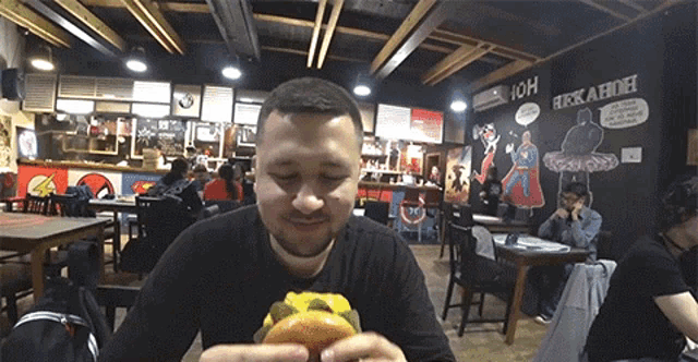 a man in a black shirt is eating a hamburger in a restaurant with a sign that says ioh on it