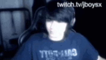 a blurry picture of a person wearing headphones and a t-shirt that says twitch.tv/jboysx .